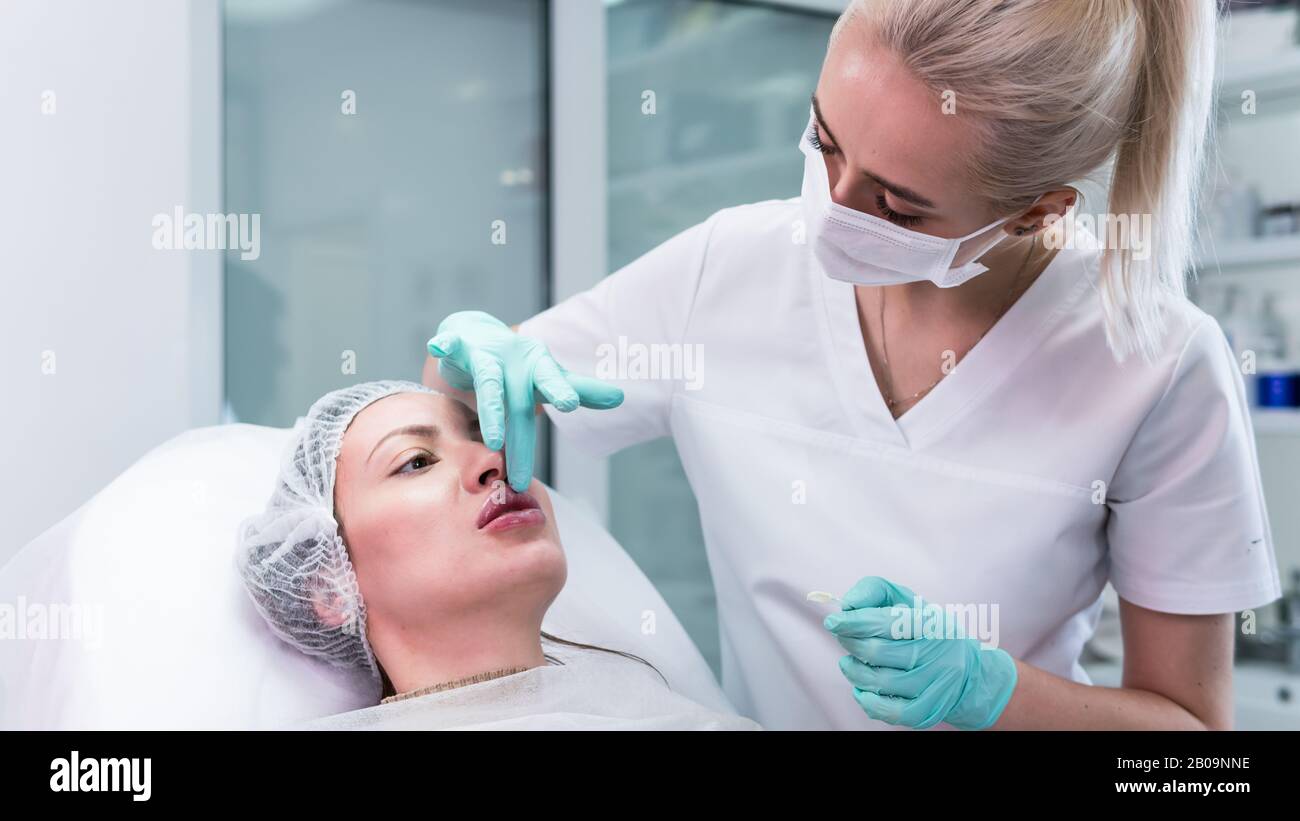 The young beautician doctor preparing to making injection in female lips. The doctor cosmetologist makes lip augmentation procedure. Concept of beauty Stock Photo