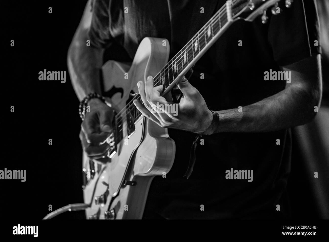 A moody black and white closeup shot on the hands of a guitar player performing during a folk music set at a festival celebrating traditional music. Soft focus Stock Photo