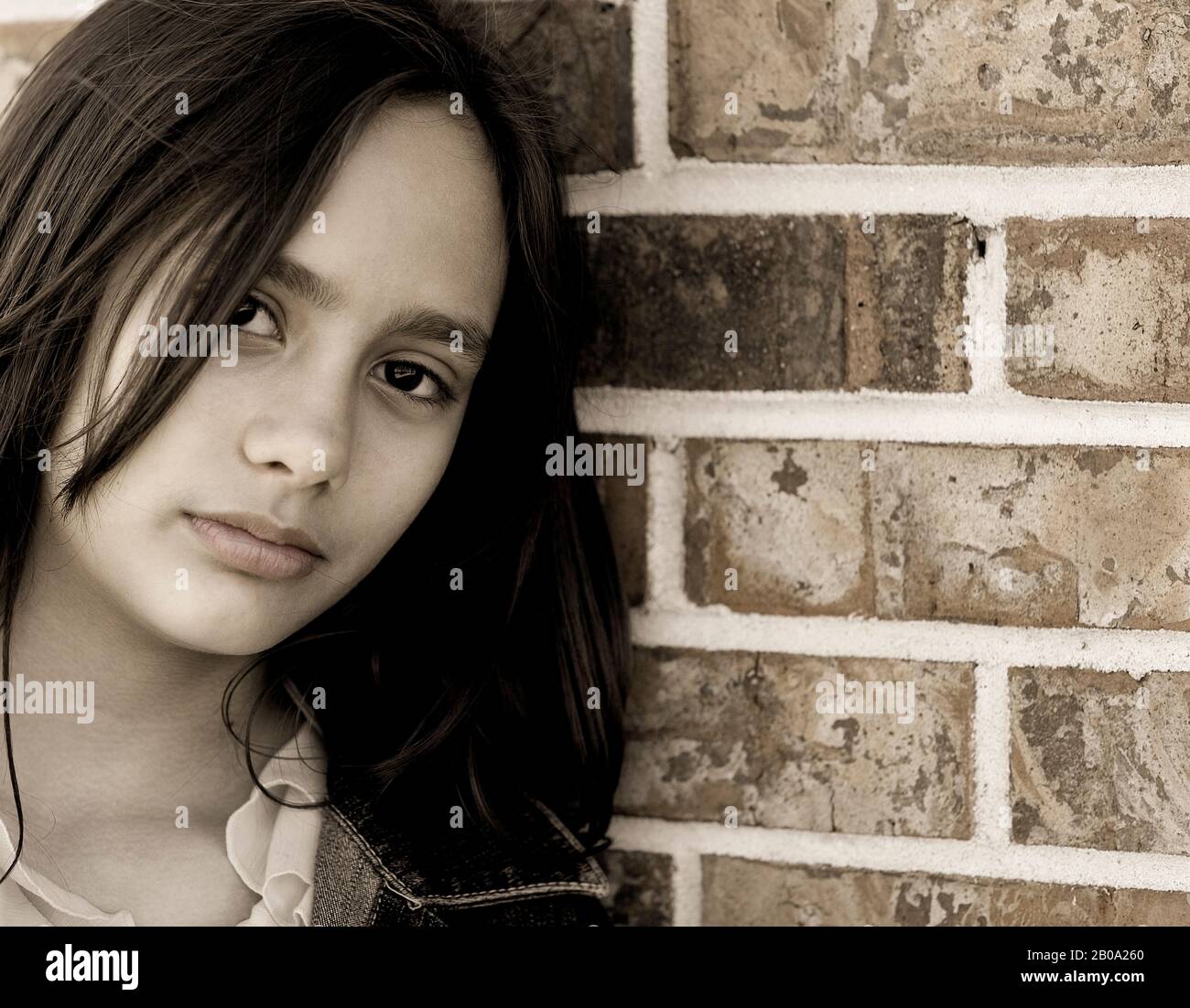 A teenage Hispanic girl with dark brown hair and eyes leaning on a brick wall. Engaged. Closeup. headshot Stock Photo