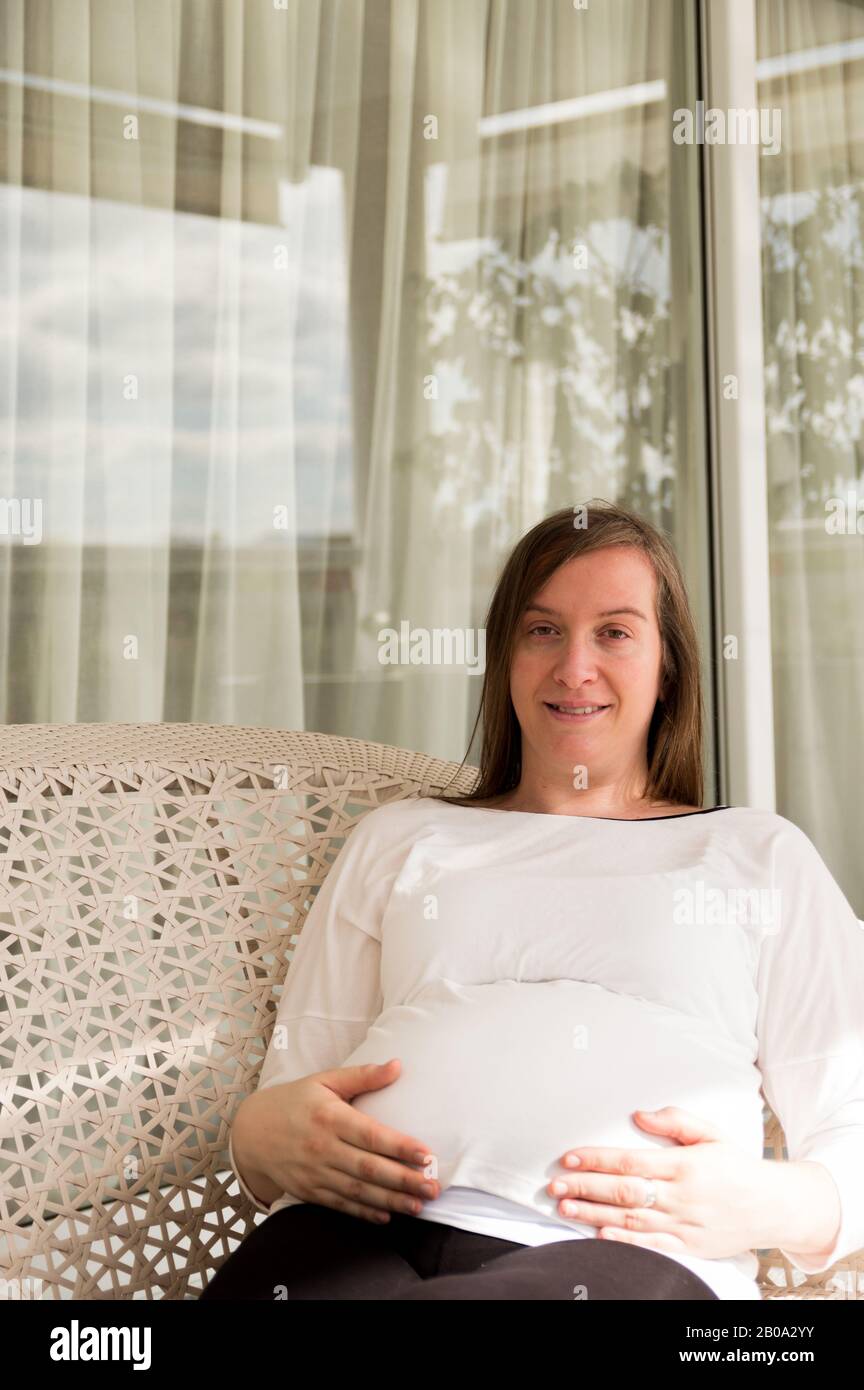 Pregnant 30 year old woman posing in an armchair in a gallery Stock Photo