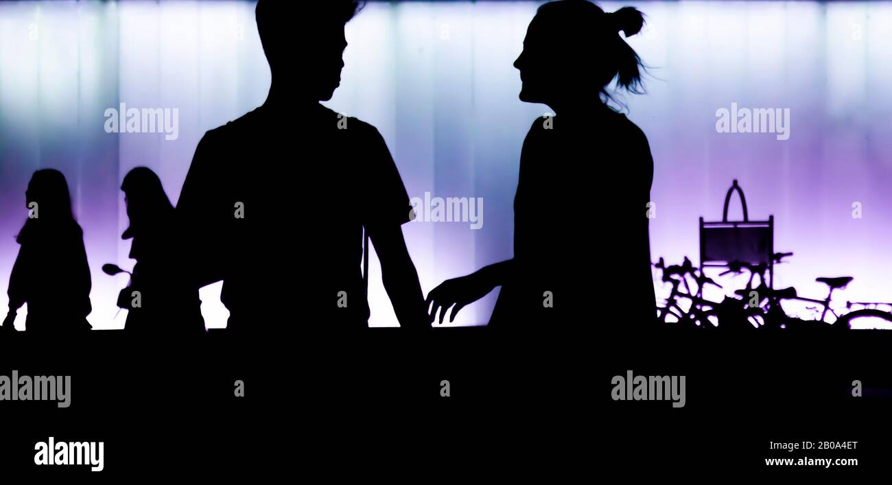Silhouettes of teen boy and girl standing in front of modern building, in the night in high contrast black and purple white Stock Photo