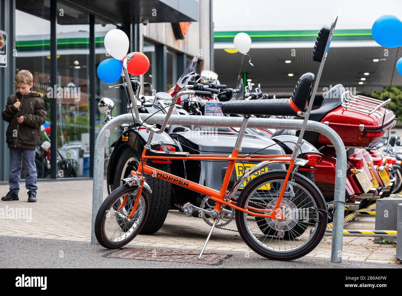 Orange 3 speed Raleigh chopper at Harley-Davidson Reading Berkshire England with kid MCC Stock Photo