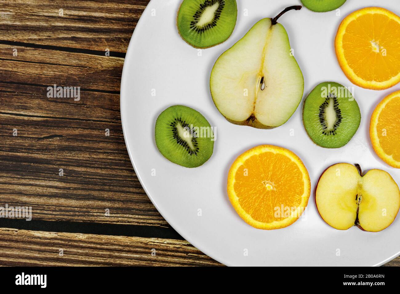 sliced fruits pear kiwi orange apple on a white plate witg rustic wooden background Stock Photo