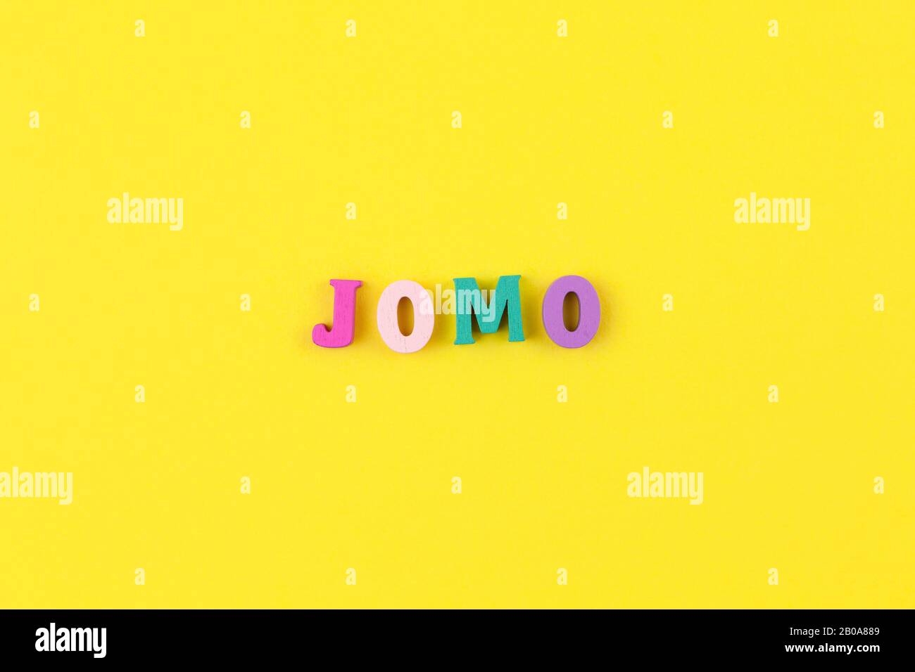 Abbreviation word JOMO in multicolored wooden letters on pastel yellow background. JOMO - Joy Of Missing Out. Opposition, choice, social problem, digi Stock Photo