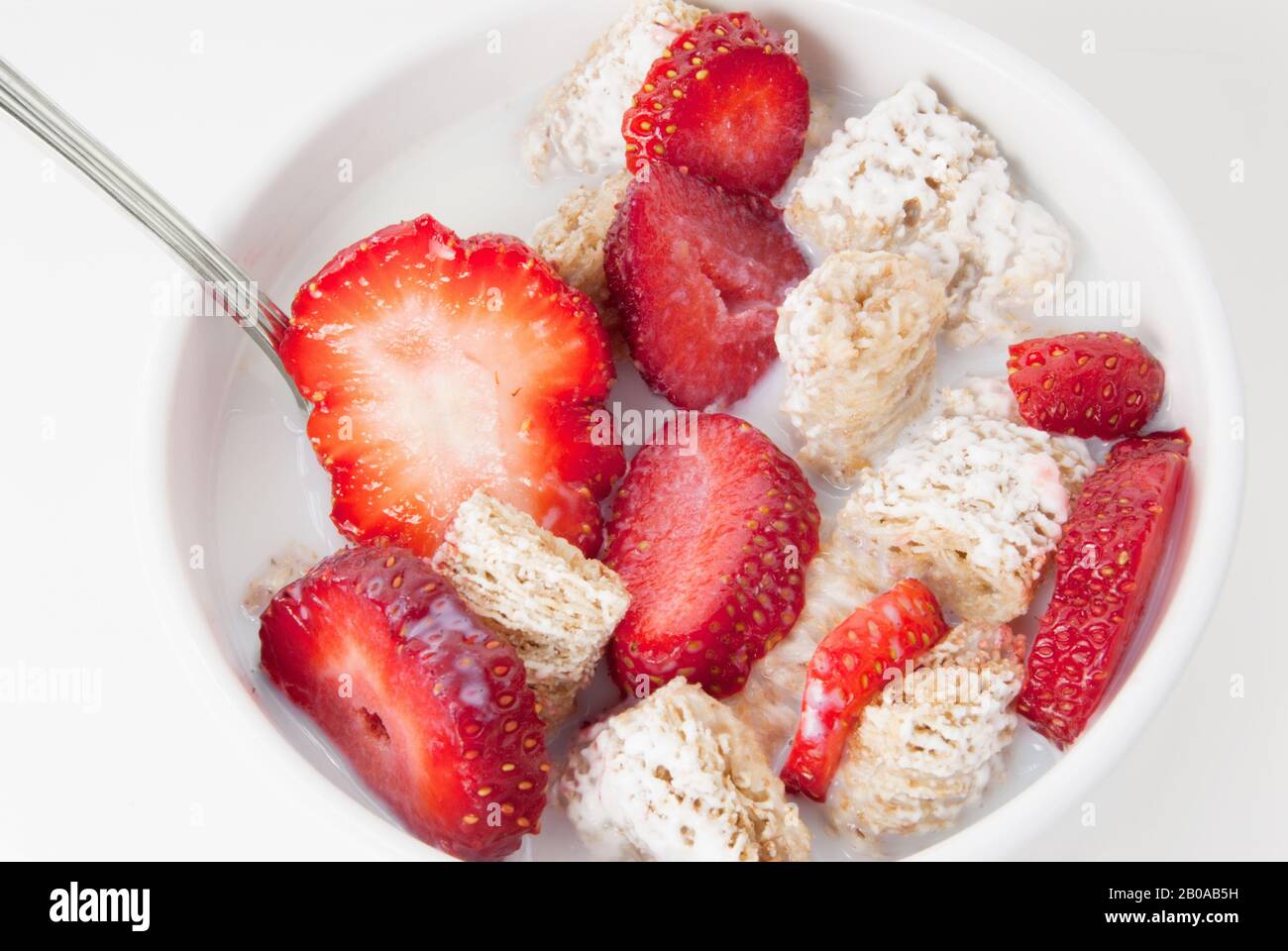 Sugar coated shredded wheat cereal served in a bowl with milk and sliced strawberries. Stock Photo