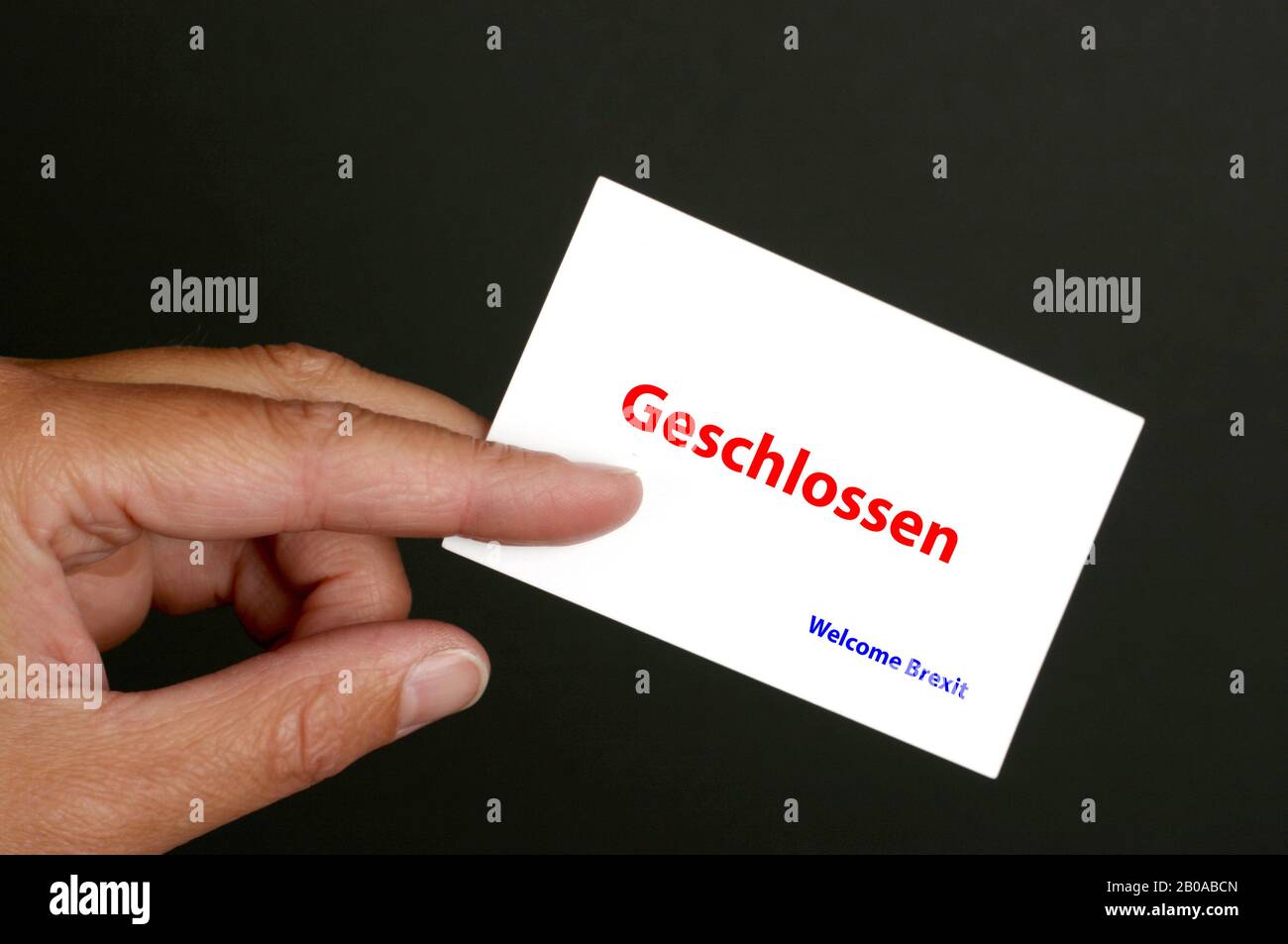 hand against black background holding card lettering Geschlossen, close, Welcome Brexit, Germany Stock Photo