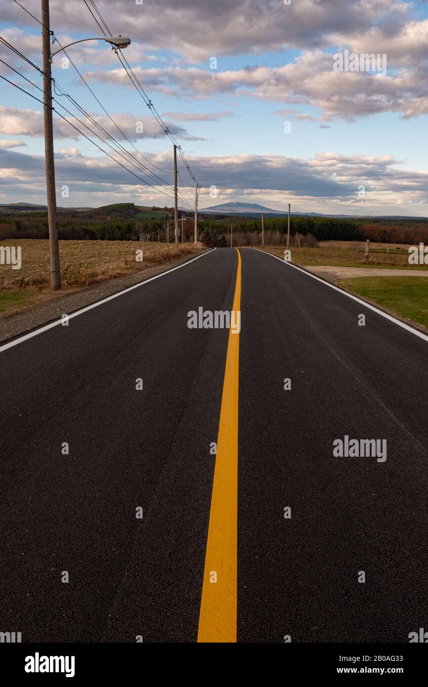 A newly paved road with a yellow line leading  us to Mt Monadnock off in the distance Stock Photo