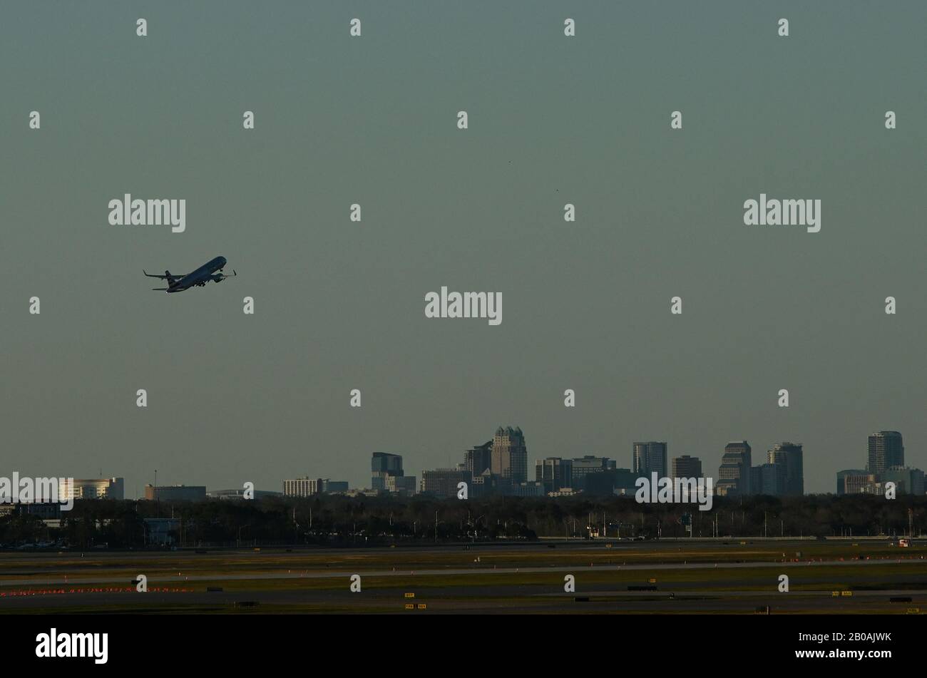 An airplane takes off at Orlando International Airport with downtown Orlando skyline in the background. Stock Photo
