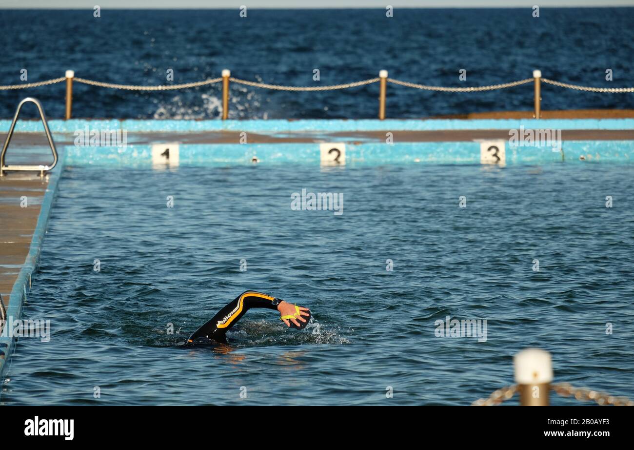 A lone man swimming laps in a wetsuit using hand paddles in an ocean