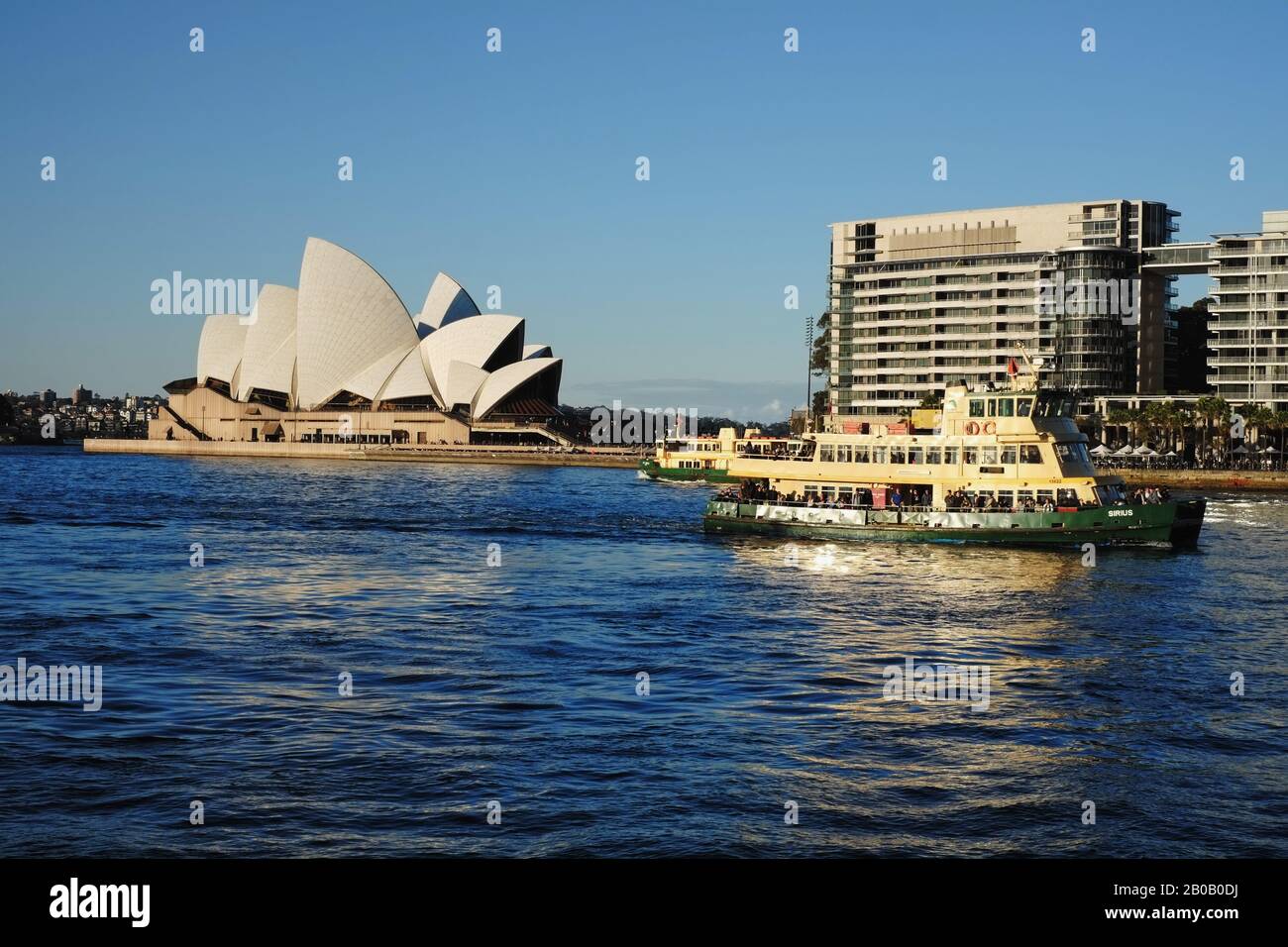 Two classic yellow and green ferries making way to Circular Quay wharf the Sydney Opera House in a soft afternoon light with a clear blue sky Stock Photo