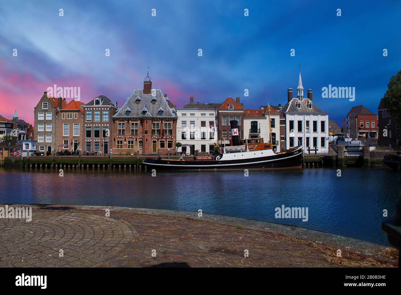 Maassluis, The Netherlands - February 21, 2018: the harbor of Maassluis with old boats, tugs and monumental houses in the evening. Stock Photo