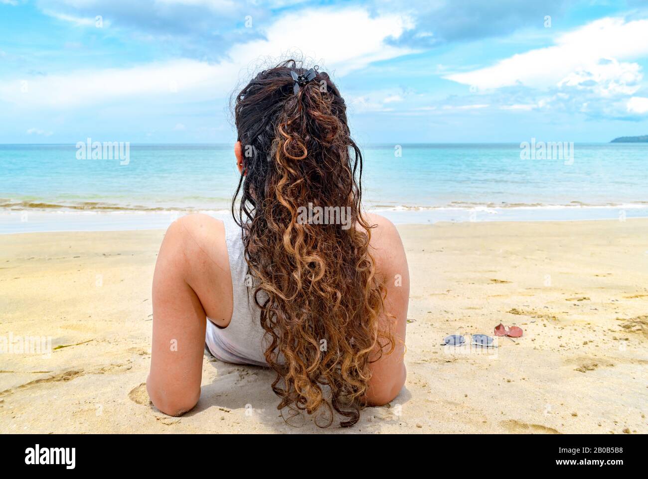Back view of attractive female model enjoying her holidays beach. She has beautiful hairstyle with colored curly hair and flawless skin getting tanned Stock Photo