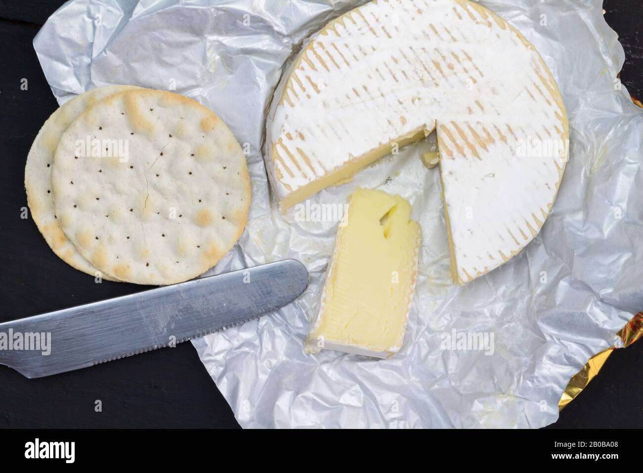 Camembert cheese whole with slice next to water crackers and knife - overhead photo Stock Photo