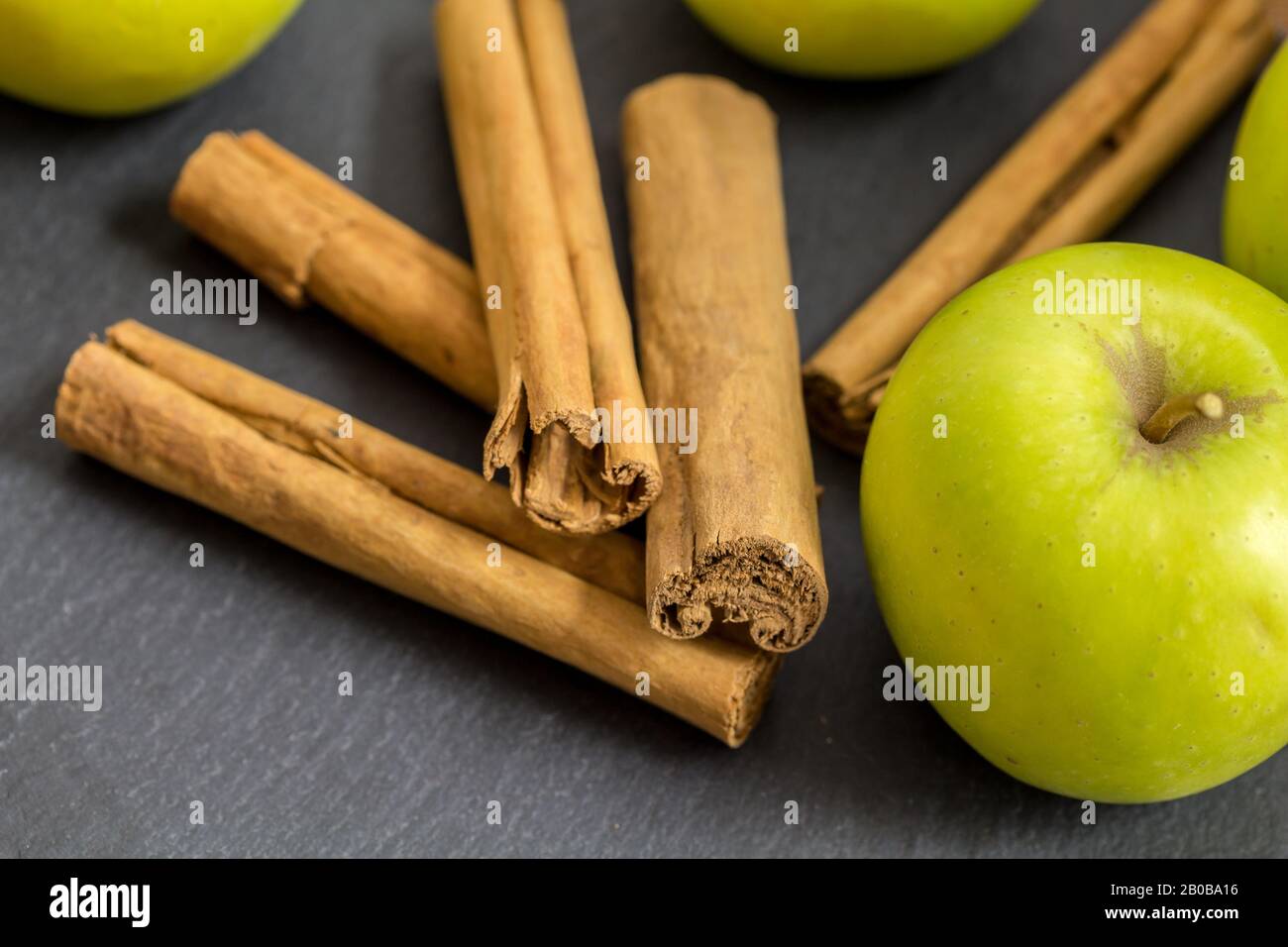 Cinnamon sticks and green apples isolated on black slate background with selective focus - close up horizontal image Stock Photo