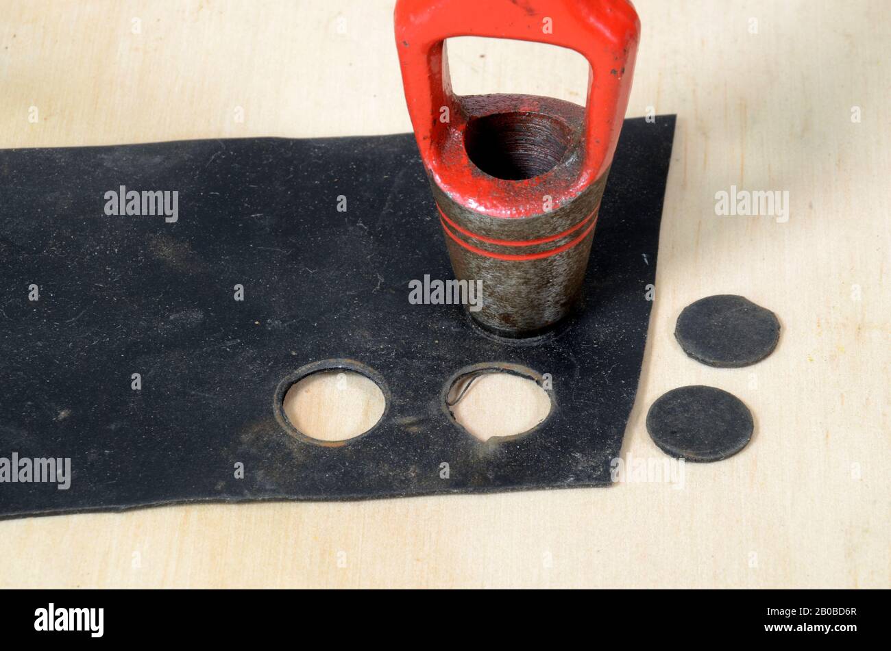 Closeup on a red hollow punch being used on a piece of black rubber to make roud gasket pieces. Stock Photo