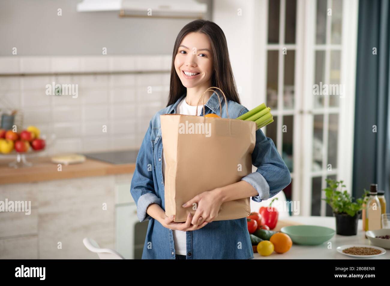 Young pretty woman standing in kitchen with an ecological bag. Stock Photo