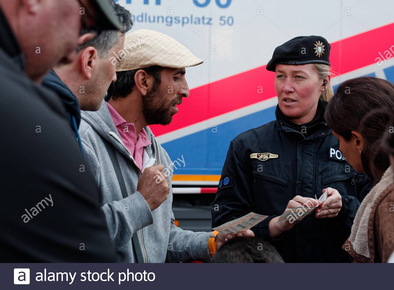 A helpful German police woman explains how to use transport tickets to newly arrived refugees outside Munich Central station in 2015. Stock Photo