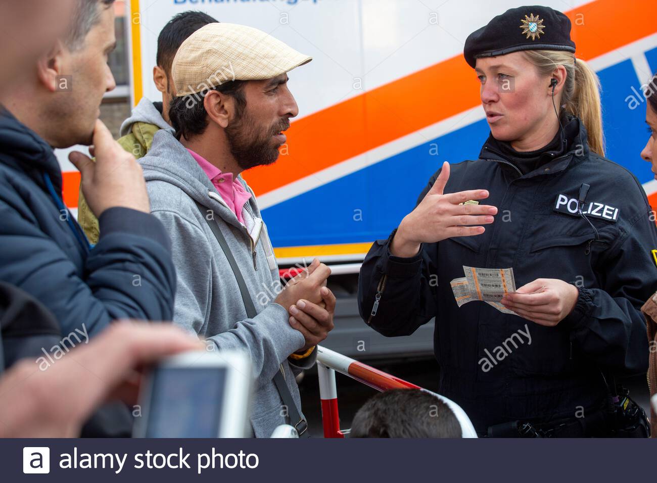 A helpful German police woman explains how to use transport tickets to newly arrived refugees outside Munich Central station in 2015. Stock Photo