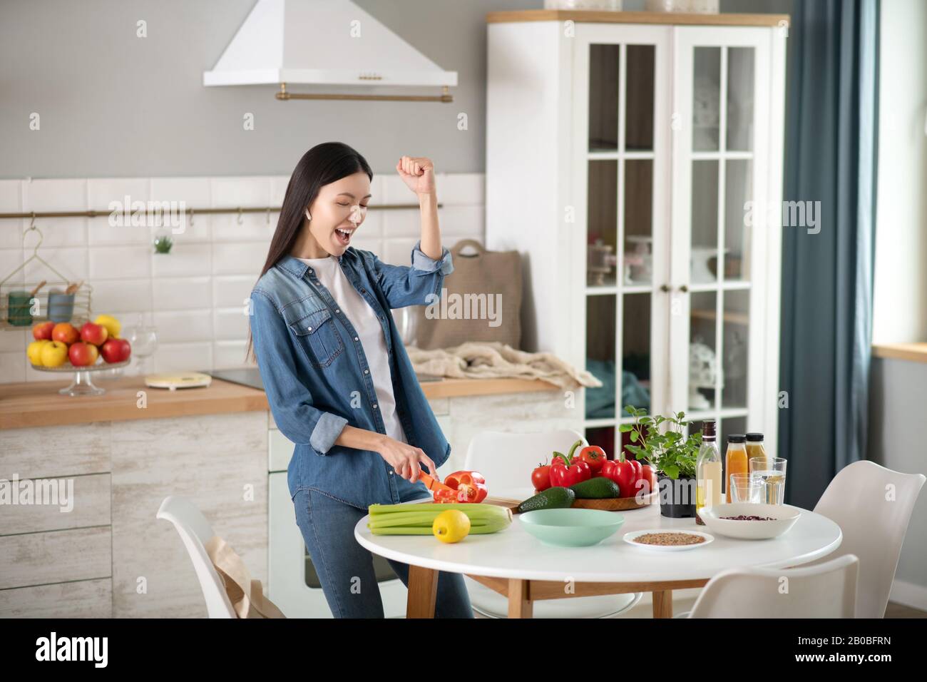Cheerful young woman slicing red bell pepper. Stock Photo