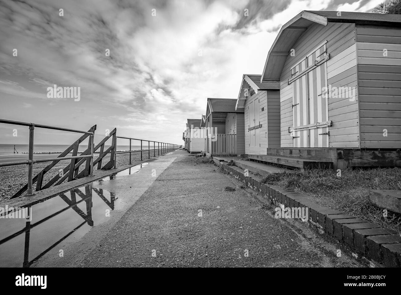 9 Row of traditional wooden beach huts on the promenade beside a sand and shingle beach on the Norfolk coast Stock Photo