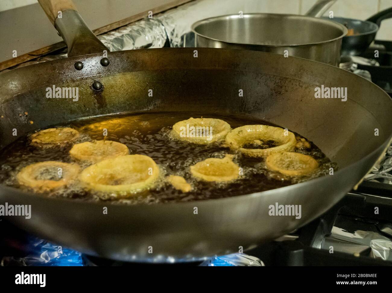 A chef deep fries Indian Pakora onion rings in hot oil over a gas stove in a restaurant kitchen Stock Photo