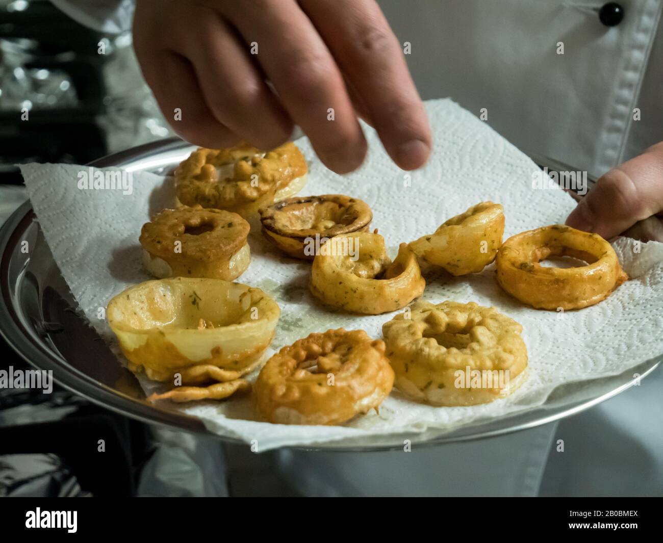 Close up of deep fried onion rings laid out onto a paper kitchen towel to dry before eating. Stock Photo