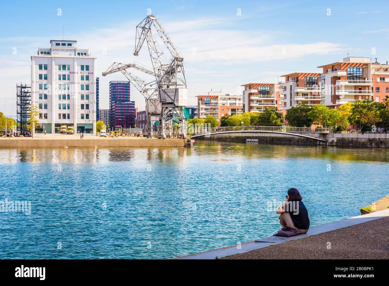 A woman sitting beside the Austerlitz basin, staring at the peninsula Andre Malraux in the new district of Les Fronts de Neudorf in Strasbourg, France Stock Photo