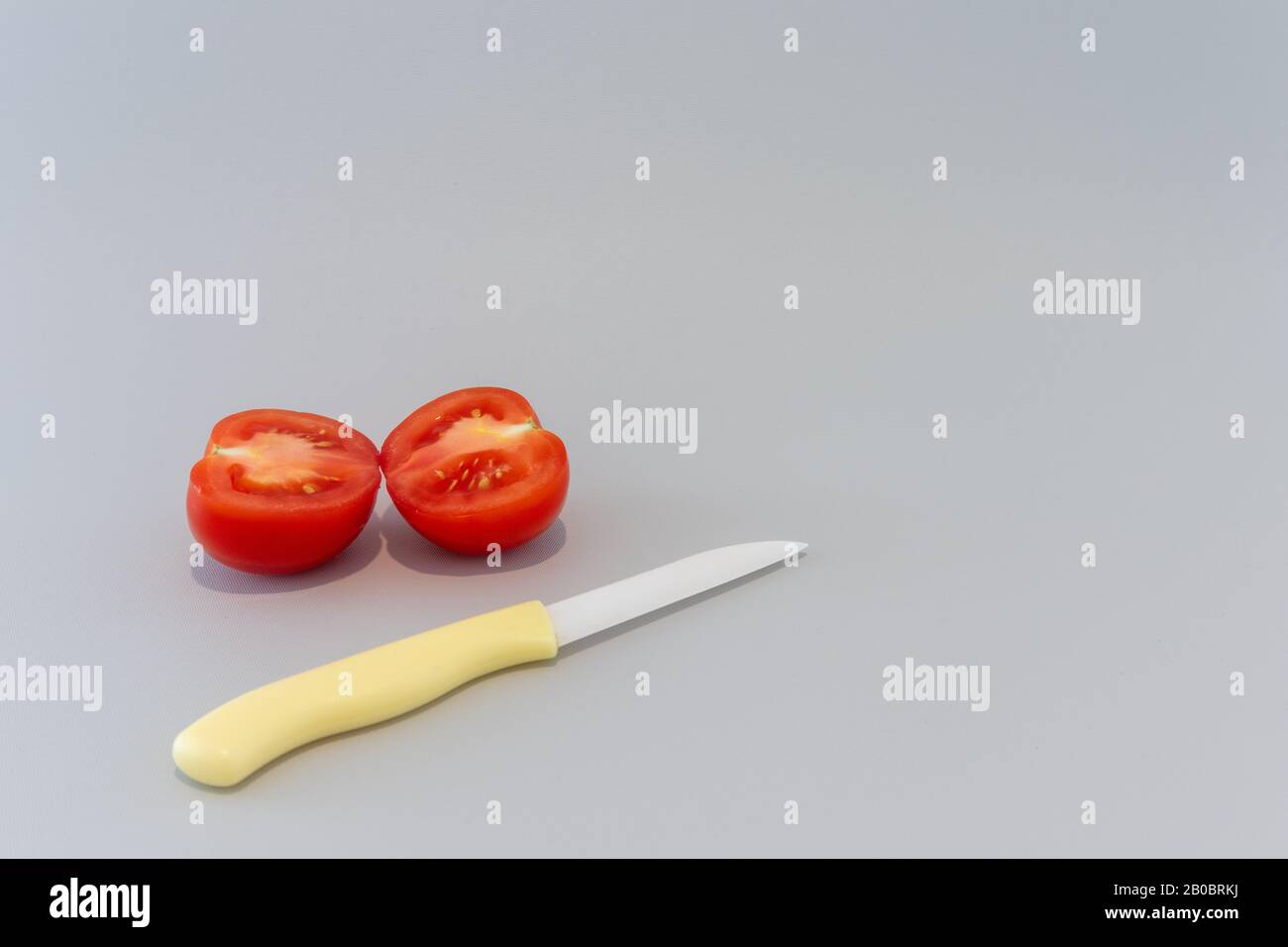 Slice tomato with yellow knife on grey background Stock Photo
