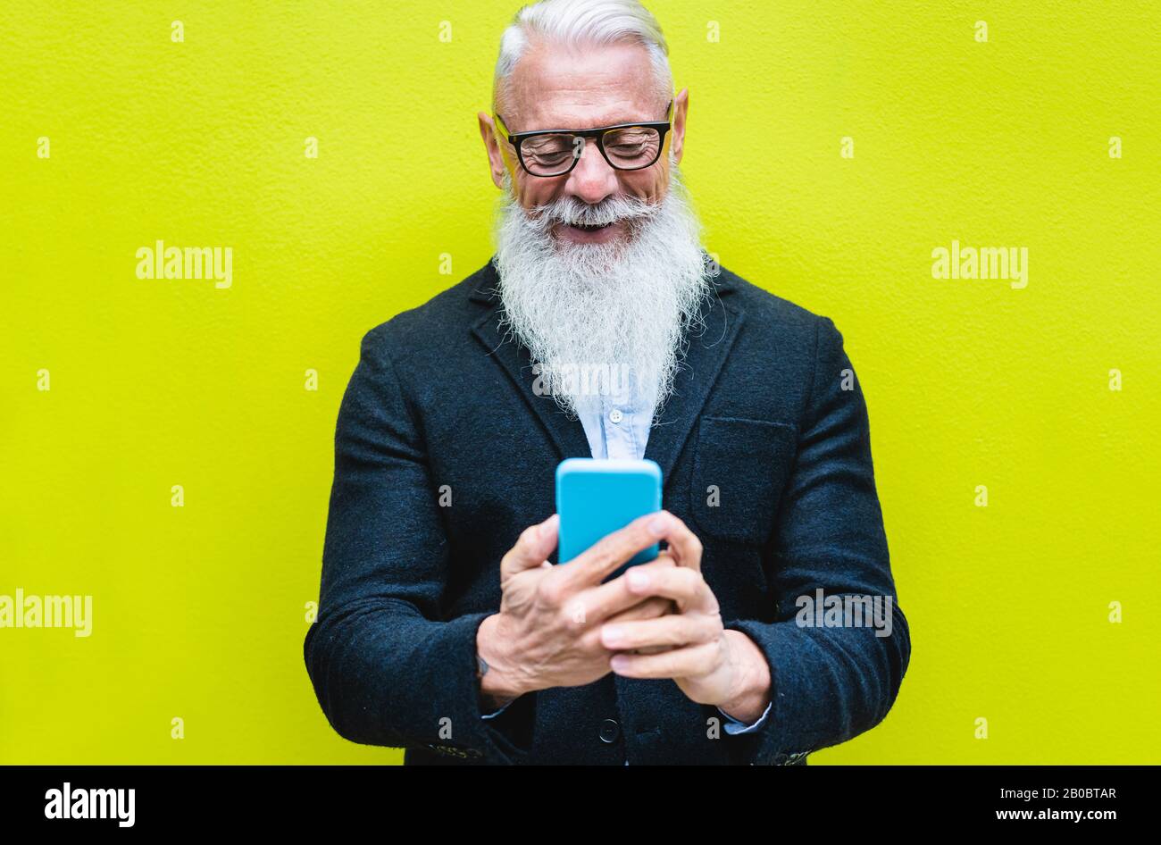 Happy senior man using smartphone app with fluorescent color in background - Hipster old guy having fun with technology - Tech and joyful elderly conc Stock Photo