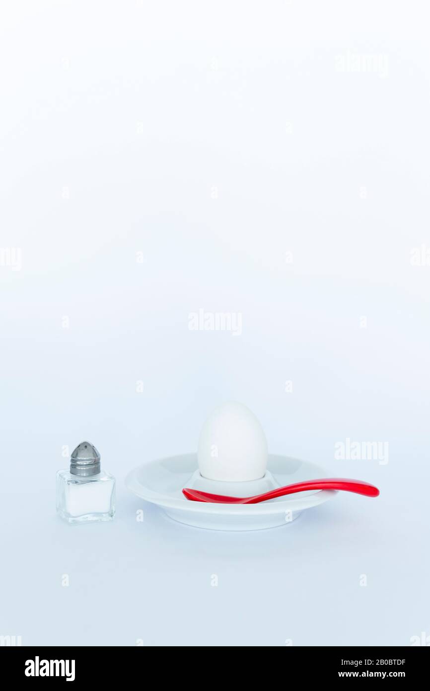 Simplistic breakfast concept with a boiled egg, a salt shaker and a spoon on white background Stock Photo