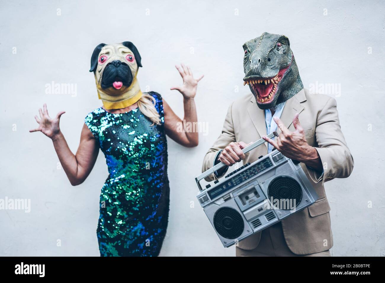 Crazy senior couple dancing for party wearing t-rex and chicken mask - Old trendy people having fun listening music with boombox stereo - Absurd and f Stock Photo