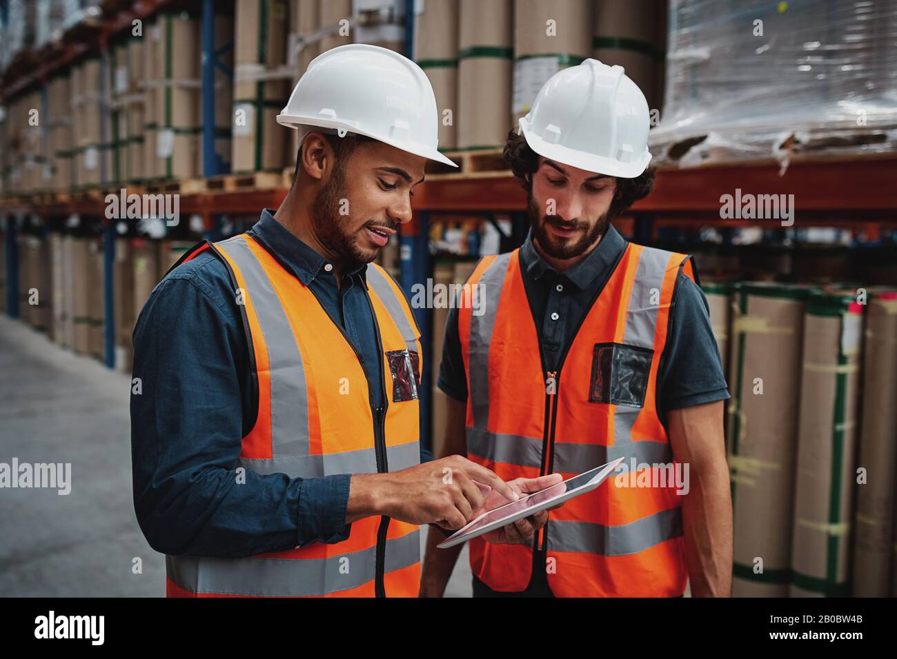 Young focused workers in warehouse discussing work on digital tablet Stock Photo