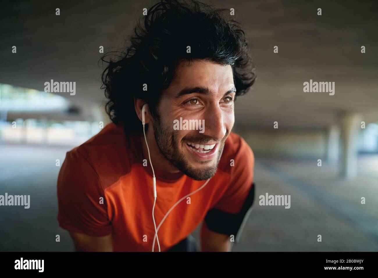 Close-up portrait of a exhausted fit young happy man with earphone in his ears taking break after jogging in the park - new year resolutions Stock Photo