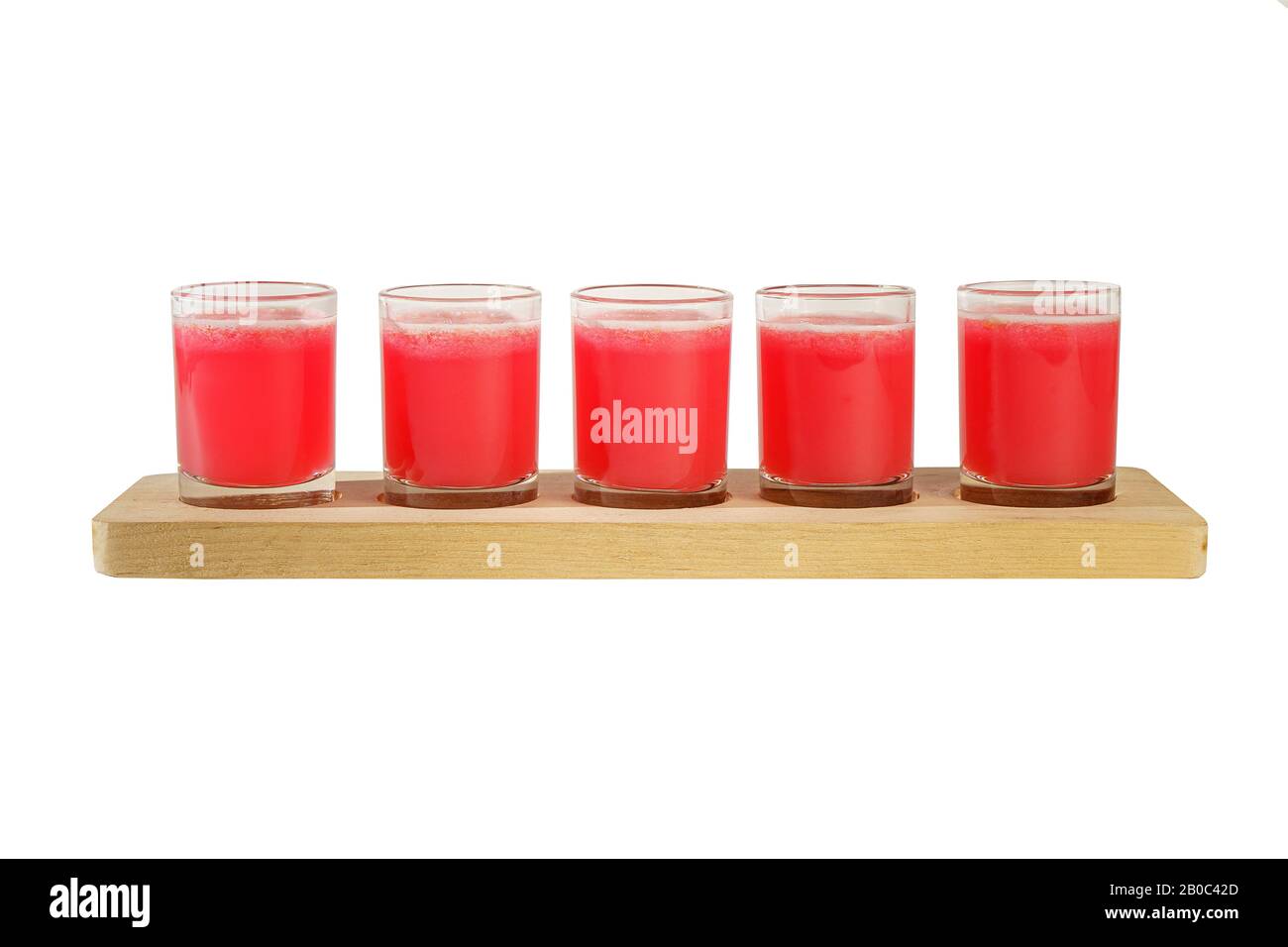 Red, same color transparent cocktails, a set of shots in one row, five servings on a wooden stand, substrate. Side view Isolated white background. Dri Stock Photo