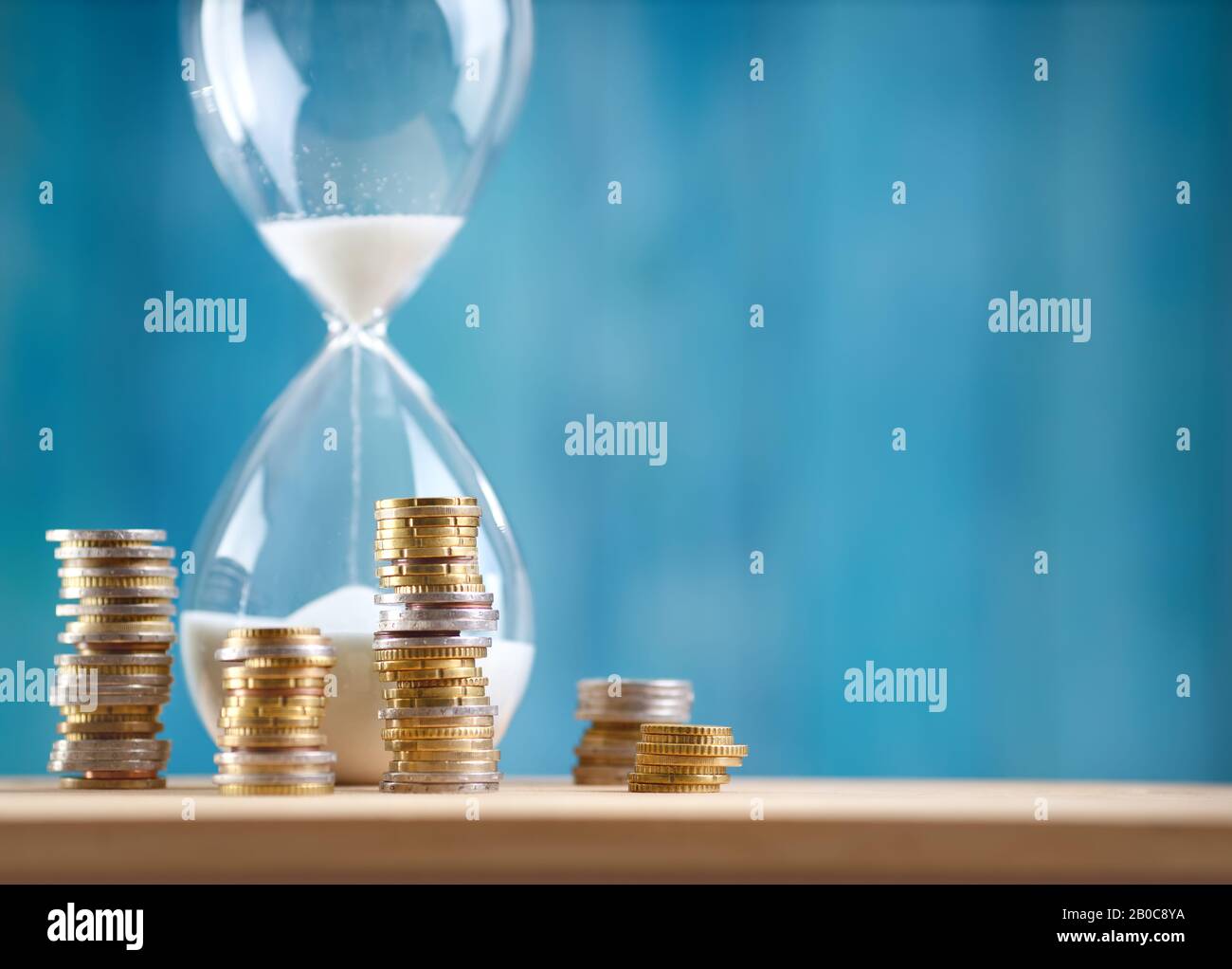 clock with stacked coins and hourglass on blue background Stock Photo