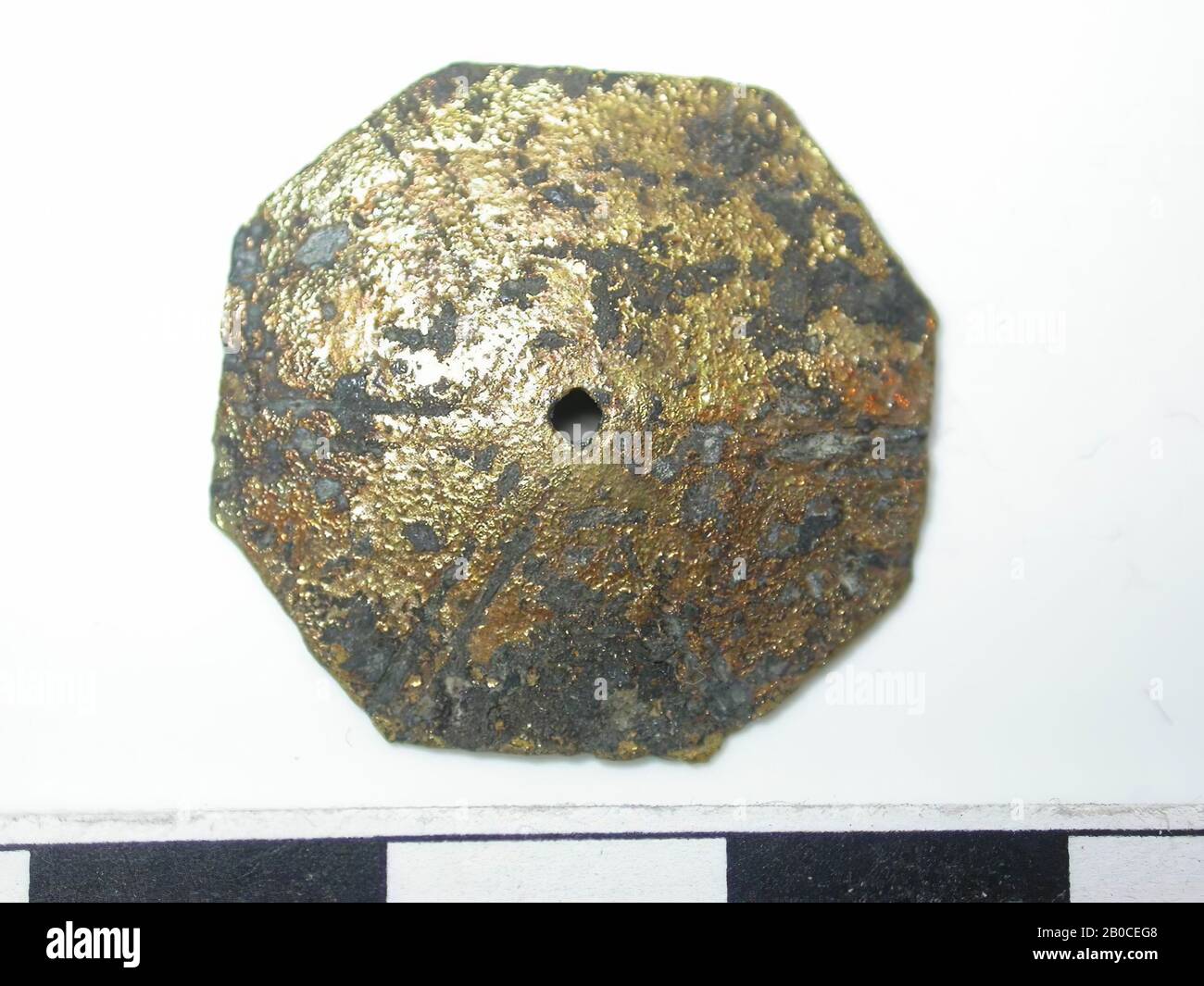 Octagon shape, golden with dark spots (copper alloy). Octagon shape with a hole in the middle. Diameter hole is 0,1 cm. Two lines run from the middle to the eight corners. Surface is weathered. Back is hollow. No confirmation visible., Belt stroke, metal, copper alloy, Dm: 2.35 cm, D: 0.2 cm, end of the 14th century 1350-1400, Netherlands, Zeeland, Hulst, Verdronken Land Stock Photo