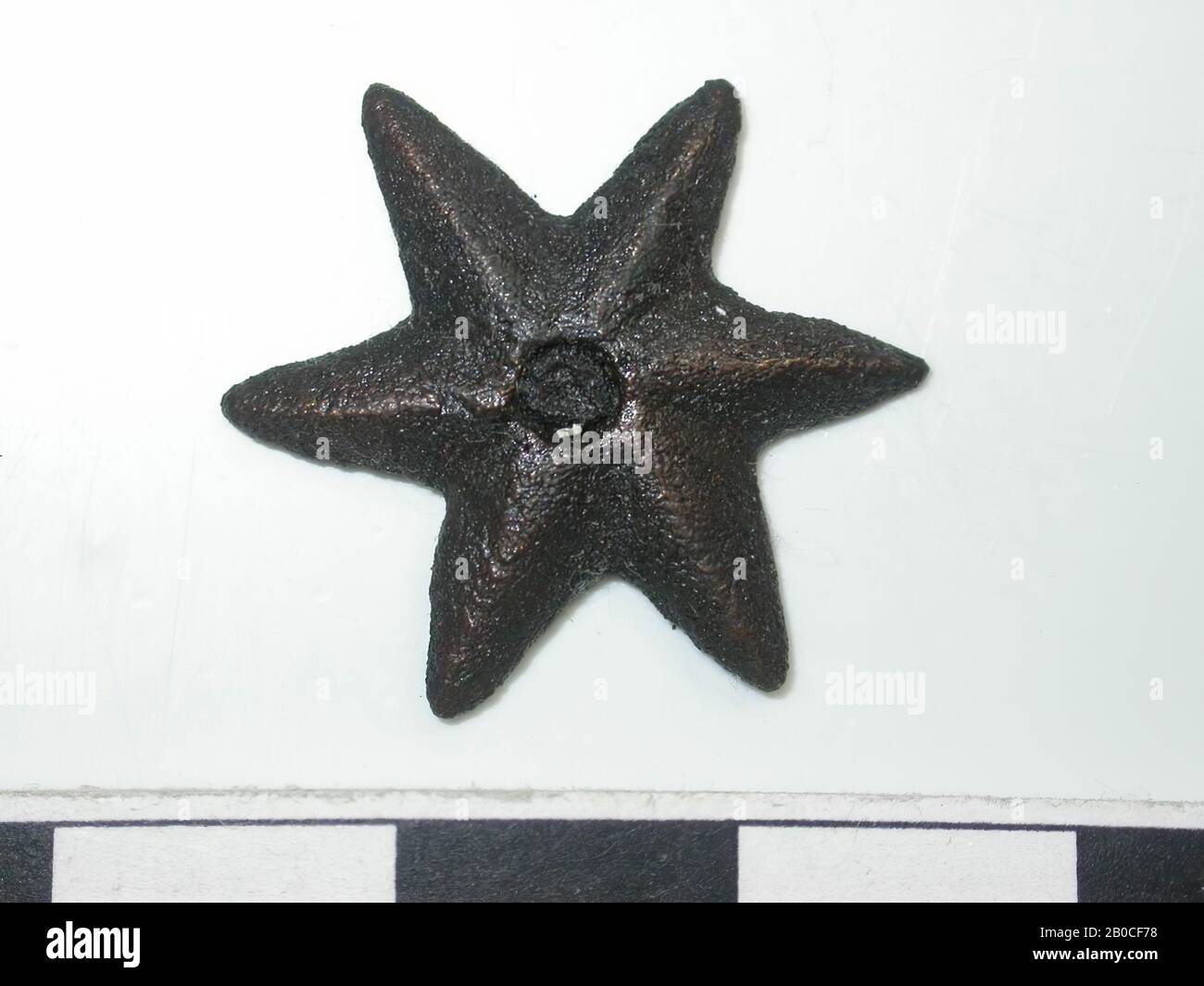 Star, gold-colored, red with dark spots (copper alloy). Star with 6 points.  A pin is stuck in the middle. Back is flat. 1 pin attachment. Pin is round.  Length is not measurable.