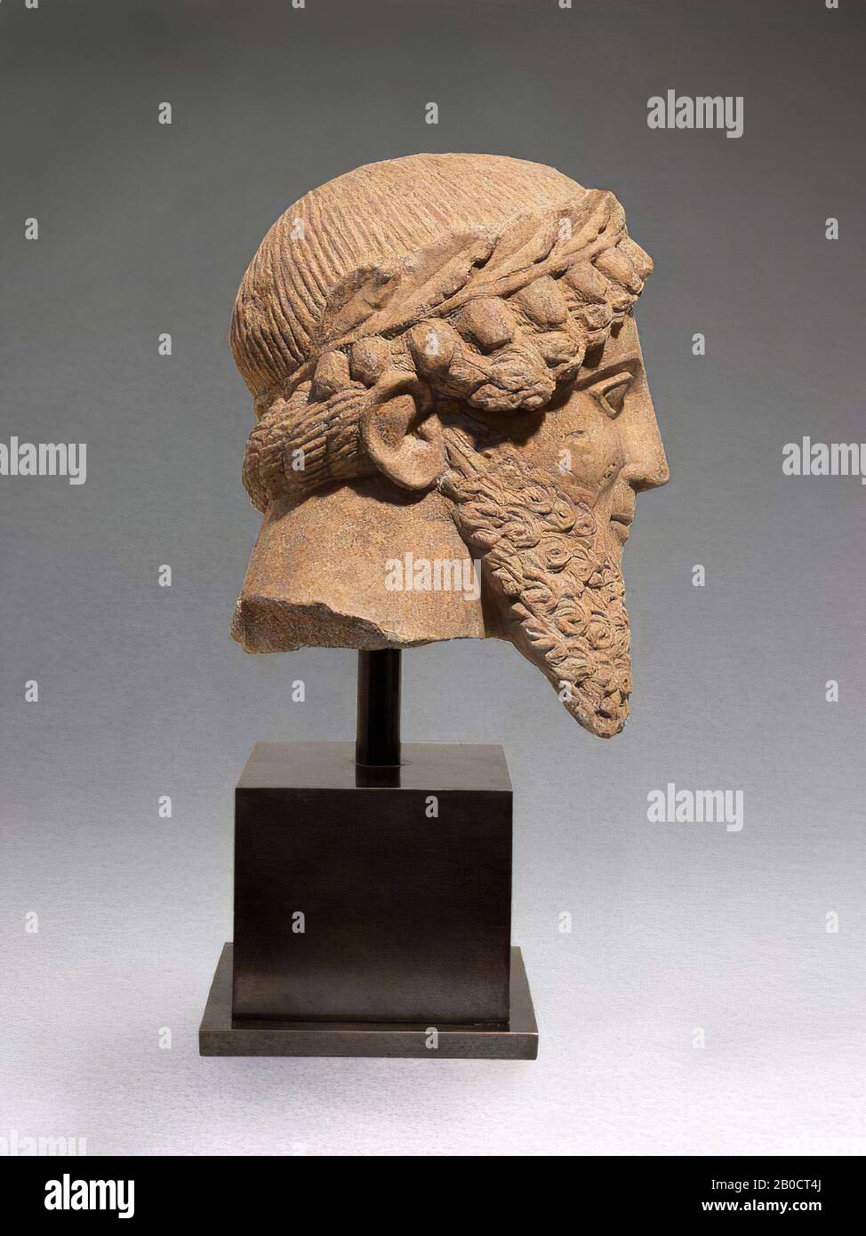 The portrait head is made of Cypriot limestone, and was originally part of a standing, male figure of life size. Such images have been found at ancient sanctuaries in Cyprus and are generally interpreted as votive gifts. The full, square beard is modeled in a symmetrical wave pattern, in contrast to the mustache, which consists of thin parallel lines. Around the mouth there is a slight smile, which is borrowed from the Greek art of the archaic period (6th century BC). The nose is straight, the eyebrows bent and provided with a sharp profile. The eyes are almond-shaped. Over the hair is a large Stock Photo