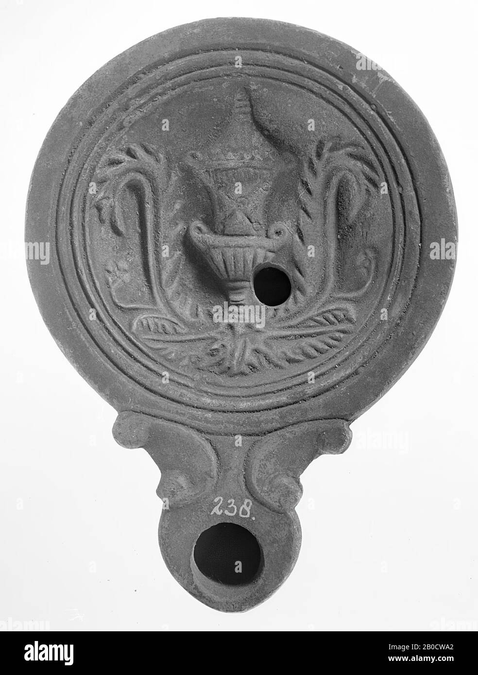 A brownish-cut oil lamp with a round body on a flat base. The hollow mirror is surrounded by recessed concentric circles and is decorated with an image of a burial mound with an acanthus leaf on either side. The short, broad spout with a large fire hole is round closed and decorated with volutes. The small filling hole is located at the bottom right of the figure. Brand: saved in shape of hares, oil lamp, earthenware, terracotta, 3.1 x 11.8 x 8.7 cm, 1st and 2nd century AD. 1-200 AD, Tunisia Stock Photo