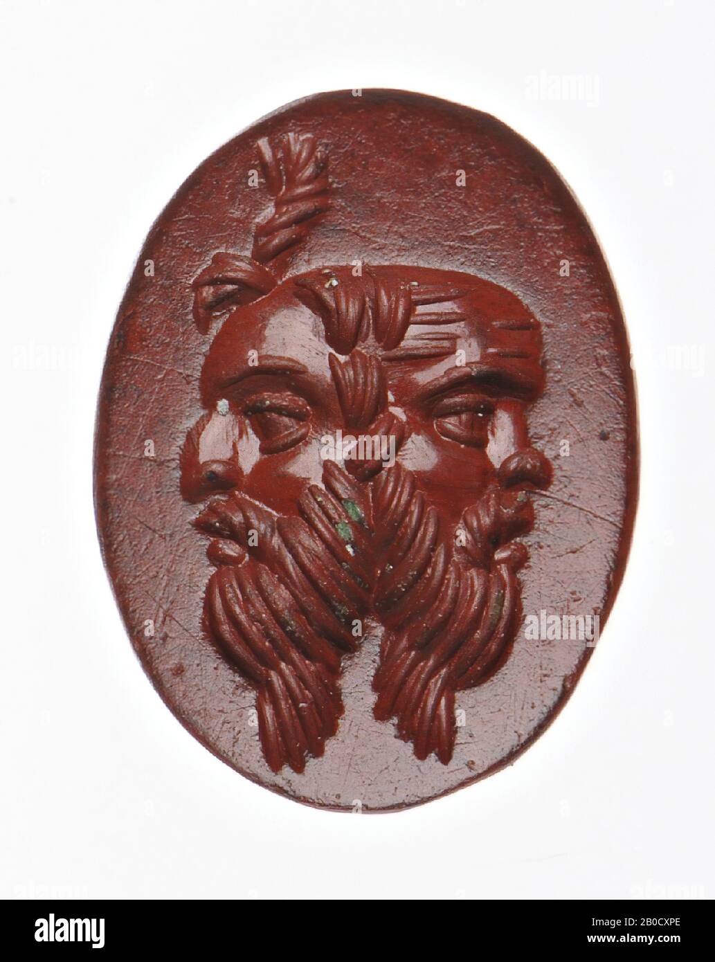 Vz: mask of a bald and bearded Silenus depicted with the back to the back of another mask of a bearded man with a strange lock of hair on his forehead., Gem, intaglio, ringstone, jasper, Color: red , Shape: oval, Machined: edge cut at the back with respect to the front, Method: modeling with rounded drill, detailing with parallel rounded wheel grooves., 12 x 9 mm, D. 3 mm, 1st - 2nd century AD . 1-200 AD Stock Photo