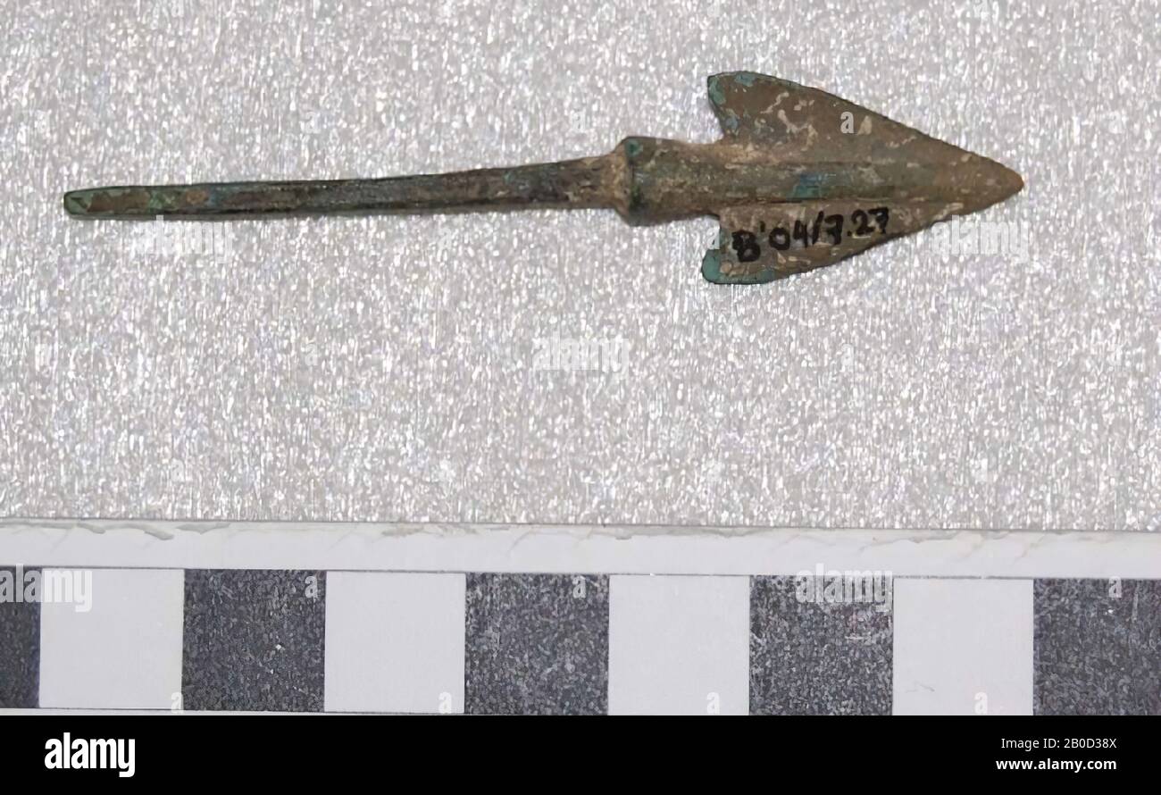 The underside of the arrowhead consists of a handle. Above the handle there is first a thickening (as if a sleeve has been pushed over it) that runs to the point. Above the thickened handle the blade starts on two sides. It first forms two recoil points (barbs) and then runs tapered to the point. The arrowhead is largely covered with light yellow and white deposits and shows light green corrosion at a single location. The origin is according to the accompanying documentation of mr. Baker Anatolia. The date is probably 2nd millennium BC, weapon, metal, bronze, L 6.9 cm, W 1.5 cm, L stem 4.1 cm Stock Photo