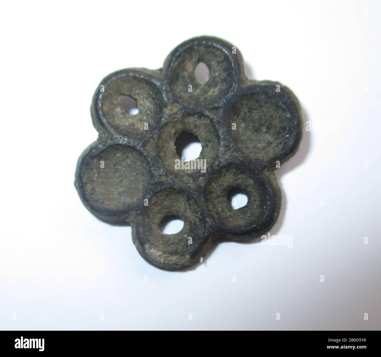 Flower with 5 leaves, interspersed with 5 pointed protrusions. In the middle a tubular hole, the bottom edge of which has been turned over (this was once confirmed by the leather). Diameter is 1.65 cm. Thickness is 4.5 mm., Belt stroke, metal, lead Stock Photo