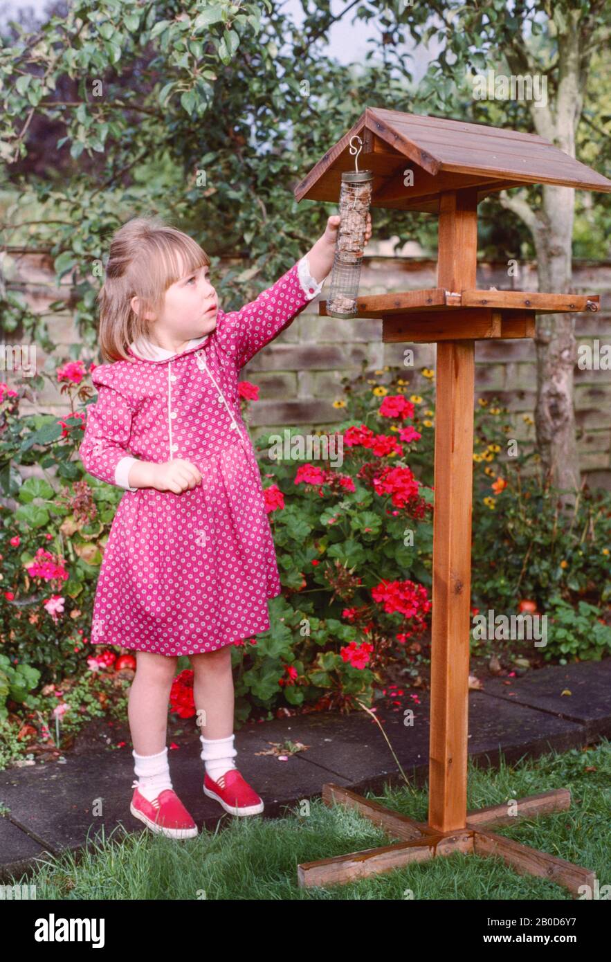 little girl putting out bird food at a bird table in a garden with
