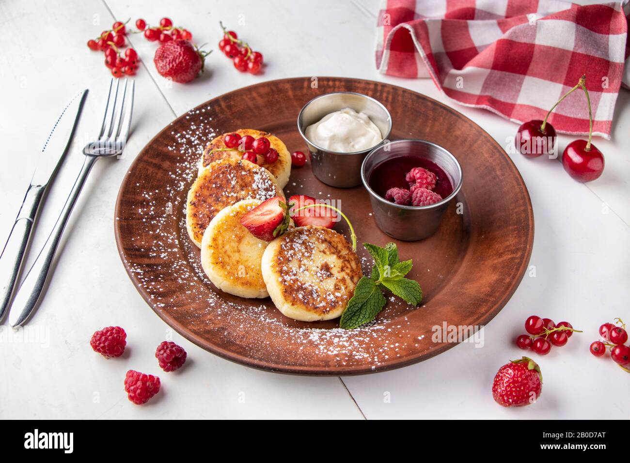 Cottage cheese pancakes, homemade traditional Ukrainian dish syrniki with berry sauce and sour cream on a brown plate on a white background Stock Photo