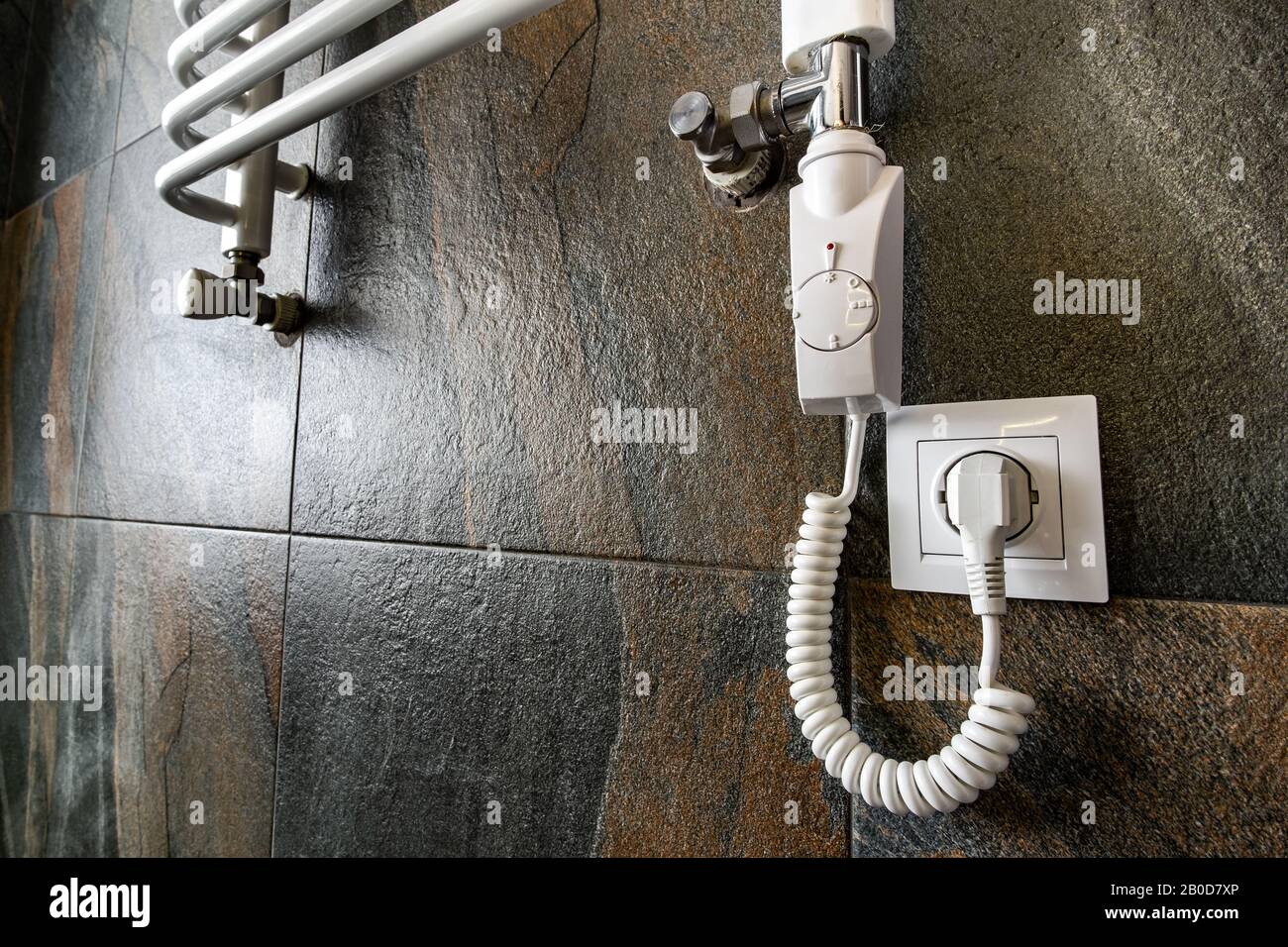 White contemporary electric towel dryer mounted on black tiled wall in