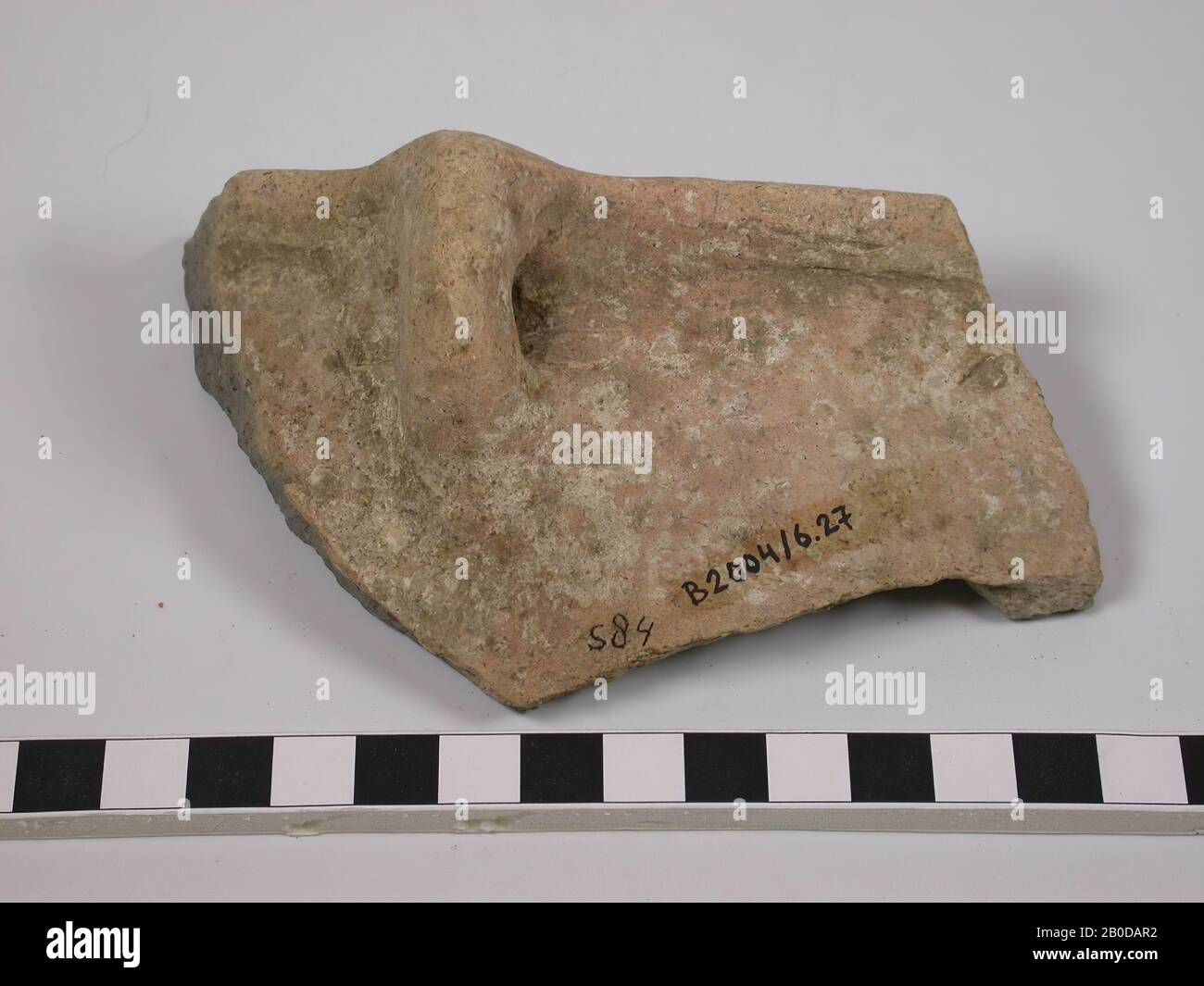Fragment of the edge and handle of a deep pot. The handle is relatively small in relation to the pot. The cross-section of the edge is a V-shape which produces a trench in the middle of the edge. The wall runs slightly bulging down from the edge. The color of the exterior is predominantly light red with many white spots. The inside is buff and dark gray on the edges., Tableware, earthenware, L 11.8 cm, W 6.9 cm, Roman Period 63 BC. - 324 AD, Palestine Stock Photo