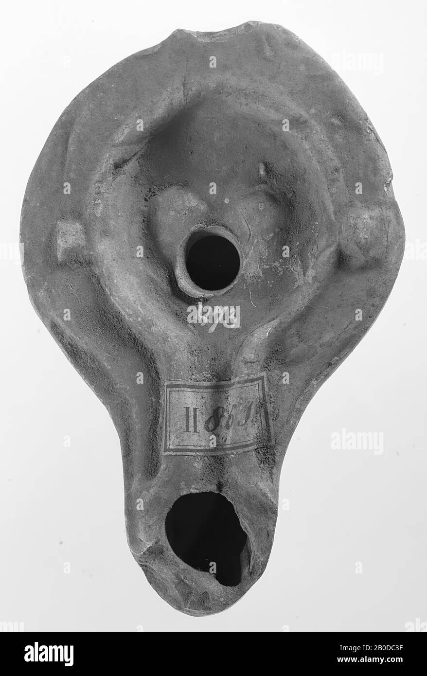 A Roughly Worked Red Earthenware Lamp With A Round Body On A Round Base The Round Mirror Is Surrounded By A High Upright Edge That Runs Over The Spout With A Small