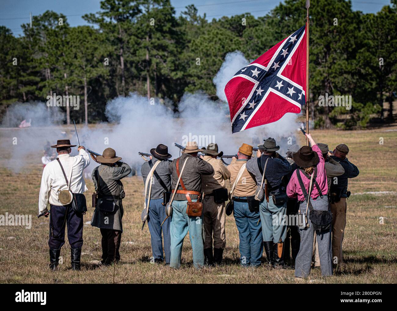 Brooksville, FL - January 18, 2020: Confederate battle flag flies over a group of civil war reenactors as they fire on the enemy. Stock Photo