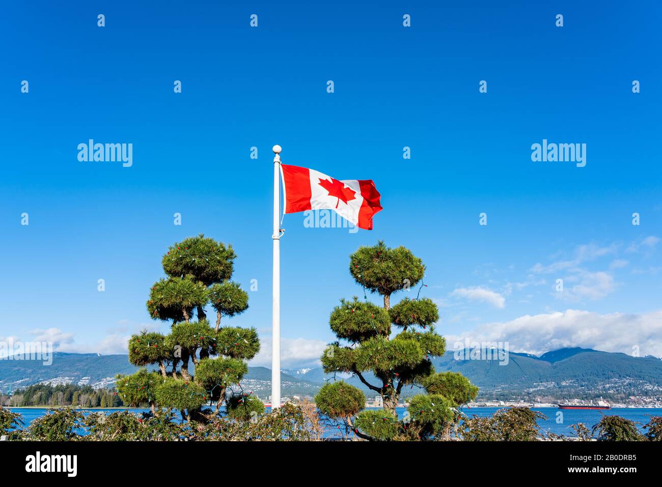 Flag of Canada flying and waving against a beautiful blue sky and a mountain view. Stock Photo