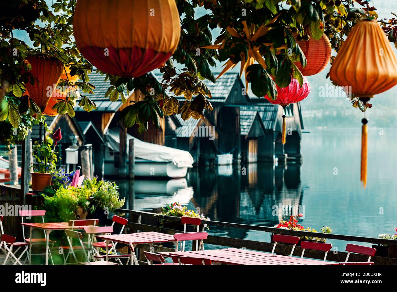 Chinese lanterns on a chestnut tree against the backdrop of an Alpine lake and boat sheds in the early summer morning Stock Photo